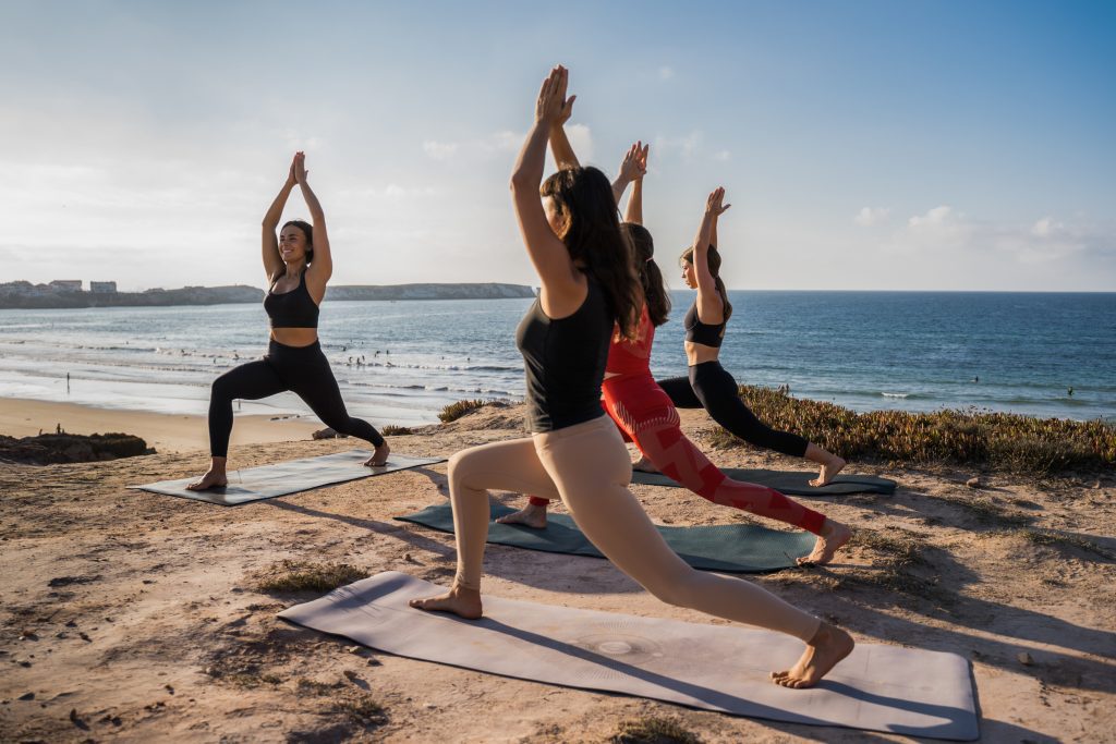 Group of young woman fitness instructor in sportswear stretching at the beach on a yoga mat with her group of students. Female fitness yoga routine concept