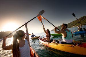 Big group of happy young friends are having fun and kayaking at sunset sea.