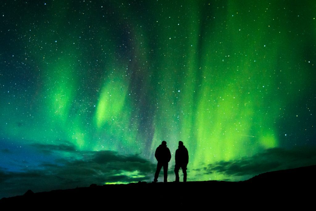 Nordlichter in Island, zwei Personen im Dunkeln beobachten den Himmel.