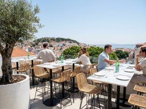 Gäste an einem Tisch auf einer Dachterrassen-Bar in Lissabon mit Panoramablick über die Stadt