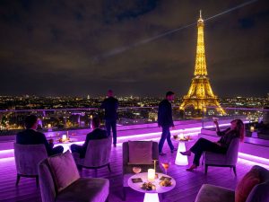 Dachterrassen-Bar bei Nacht mit beleuchtetem Eiffelturm im Hintergrund