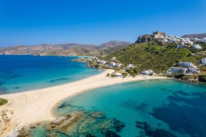 Türkisfarbene Bucht mit Sandstrand und weißem Bergdorf auf einer griechischen Insel
