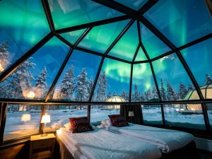 Glas-Iglu bei Nacht mit Blick auf das Nordlicht über verschneiten Bäumen