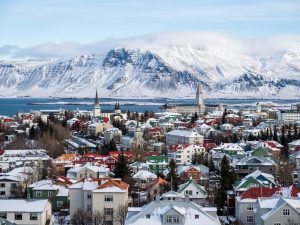 Blick auf eine isländische Küstenstadt mit bunten Häusern vor schneebedeckten Bergen