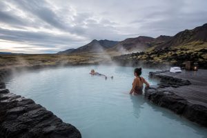 erson entspannt in einem geothermischen Thermalbad in Island, umgeben von Bergen und aufsteigendem Dampf